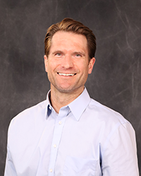 Kyle Scherr 200x250 Kyle Scherr portrait, showing head and shoulders, smiling, on a gray background