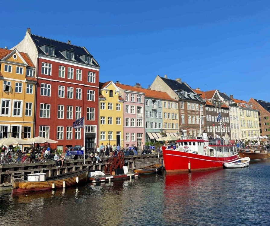 A picturesque scene of a waterfront with colorful buildings, and people enjoying the sunny weather.