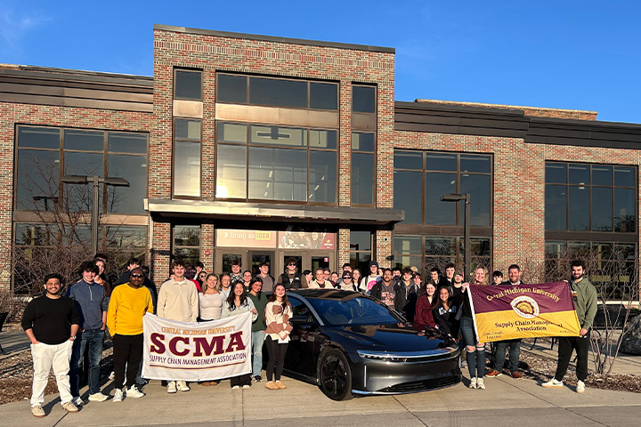 Central Michigan University students pose with a Lucid Air electric vehicle outside the College of Business Administration building during a Supply Chain Management Association event.
