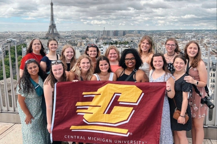 StudyAbroadAppliedLanguagesandCultures A group of students posing for a photo with a CMU flag in front of the Eiffel Tower