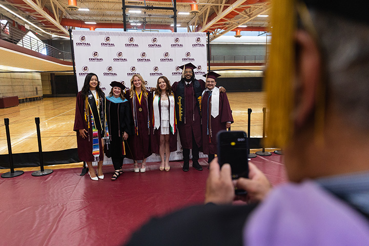 Graduates pose for a group photo in front of a step-and-repeat banner inside the SAC