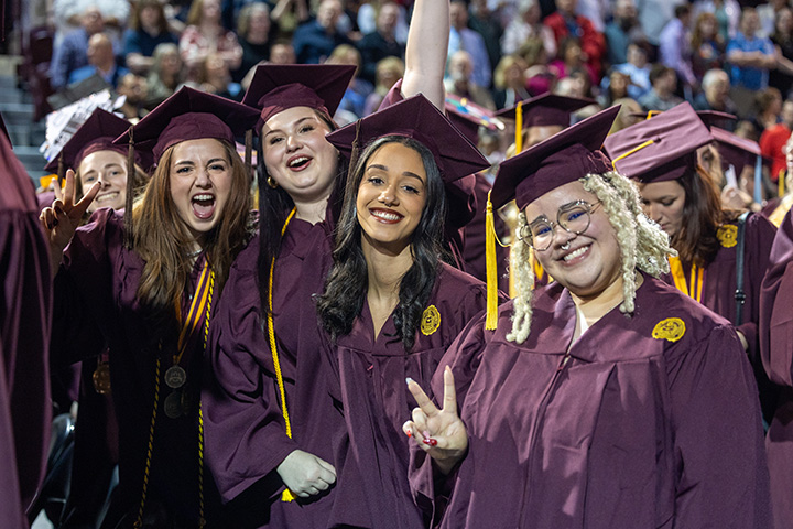 A group of female students pose for a photo in the crowd during commencement