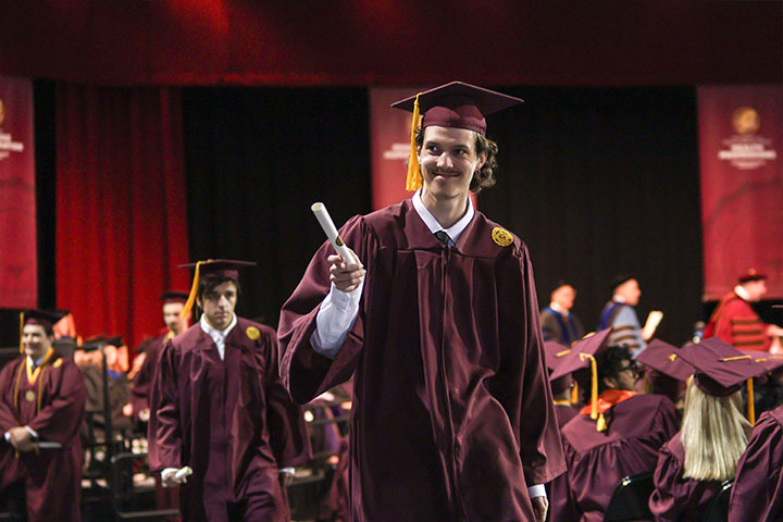 A man in a maroon robe smiling and holding a diploma.