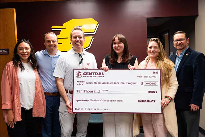 Six adults stand in front of a maroon wall with a gold Action C logo holding a large Go Grants check