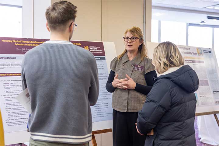 A woman stands in front of a research poster talking to two students