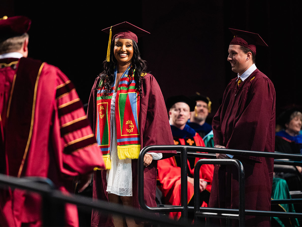 Multiple students in their cap and gown on stage at commencement