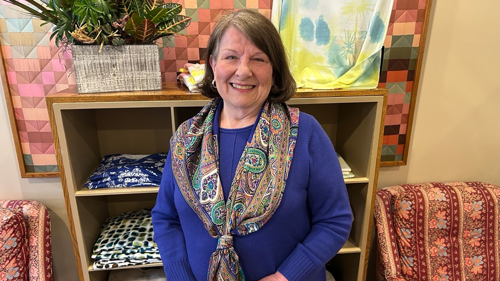 A woman wearing a blue shirt and paisley scarf is smiling.