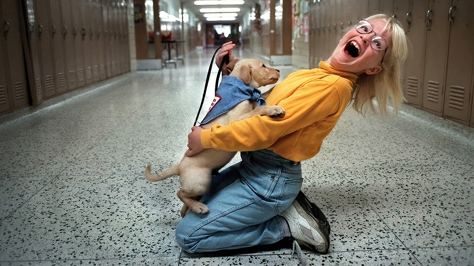 A girl kneeling on the ground holding a puppy in a school hallway.
